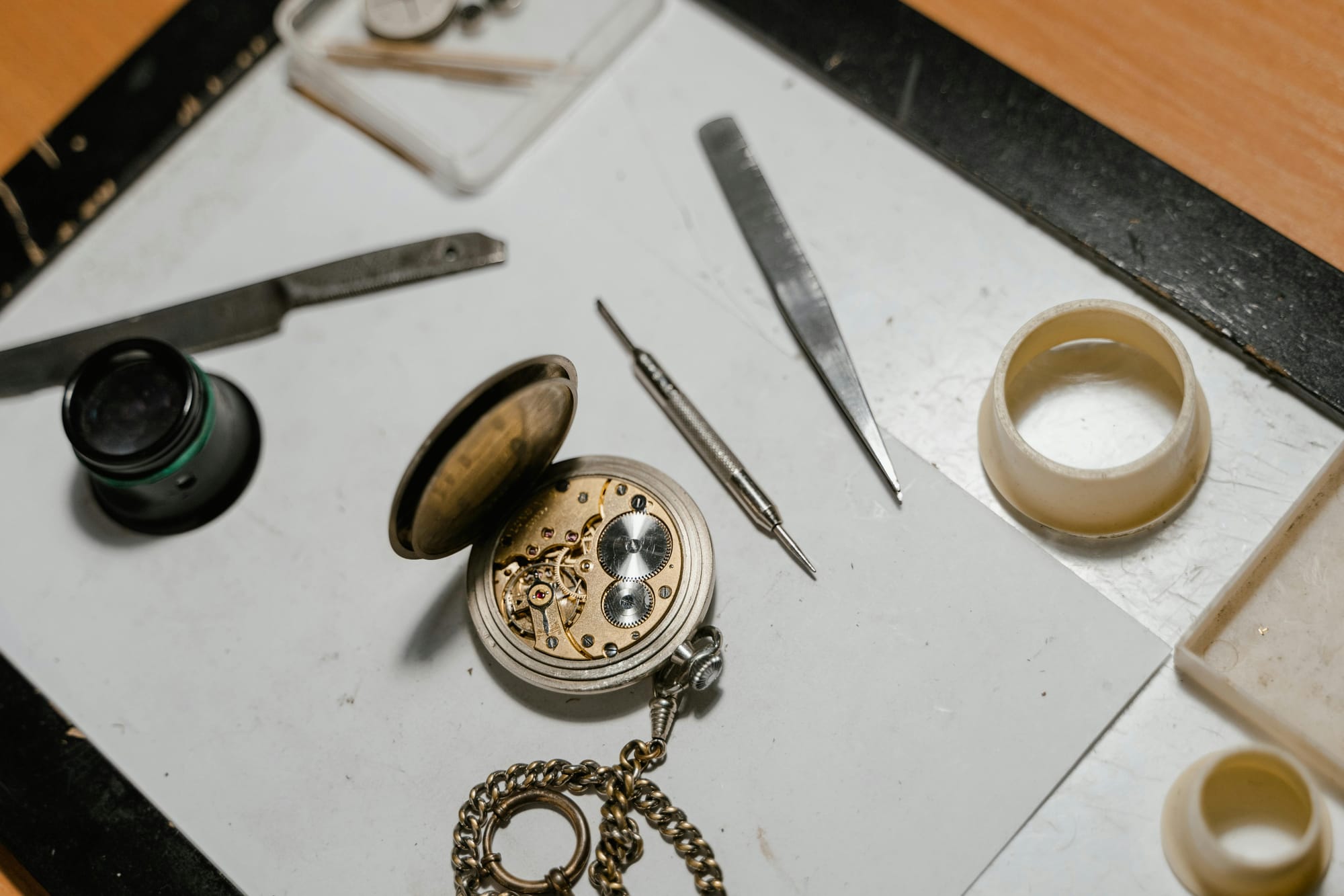 Open pocket watch with loupe, tweezers, and movement holder on a watchmaker's bench